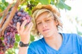 Young winemaker in straw hat examining grapes