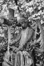 Black and white young winged angel sculpture holding a scroll in it`s hands with a big cross standing next to it. Royalty Free Stock Photo