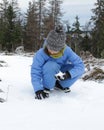 Young winter child touching snow, sitting on the ground