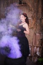 A young witch with a book in her hands cooks a potion in a large black cauldron, emitting magical purple smoke