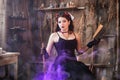 A young witch with a book in her hands cooks a potion in a large black cauldron, emitting magical purple smoke