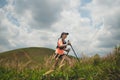 Young women active trail running across a meadow on a grassy trail high in the mountains in the afternoon with trekking pole