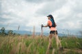 Young women active trail running across a meadow on a grassy trail high in the mountains in the afternoon with trekking pole