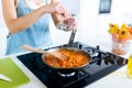 Young woman adding pepper and mixing food in frying pan.