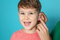 Young woman adjusting little son`s hearing aid on color background Royalty Free Stock Photo