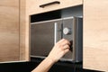Young woman adjusting modern microwave oven in kitchen