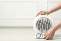 Young woman adjusting temperature on modern electric fan heater indoors, closeup. Space for text Royalty Free Stock Photo