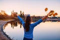 Young woman admiring autumn river scene with raised and opened hands holding branches