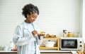 Young woman african american spreading jam on bread and eating in kitchen, student enjoys breakfast or snacks of toast with jam