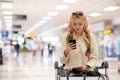 Young woman at the airport with trolley bag, talking on the phone, looking at camera and smiling. Royalty Free Stock Photo