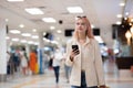 Young woman at the airport with trolley bag, talking on the phone, looking at camera and smiling. Royalty Free Stock Photo
