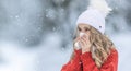 Young woman with allergy symptom blowing nose. A sick girl in a warm knitted sweater and a woolen cap using a tissue in a winter