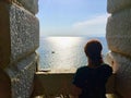 A young woman alone standing from the top of an old stone bell tower looking out at the vast ocean. Royalty Free Stock Photo