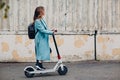 Young woman alternative commute with electric scooter in blue coat at the city Royalty Free Stock Photo