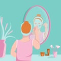 Young woman applies face mask on with brush in front off mirror