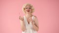 Young woman applies red lipstick on lips with makeup brush. Woman looking like Marilyn Monroe in studio on pink Royalty Free Stock Photo