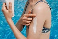 A young woman applies white sunscreen on her shoulder against the background of blue water in a swimming pool. The concept of Royalty Free Stock Photo