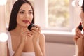 Young woman applying beautiful glossy lipstick in front of mirror indoors Royalty Free Stock Photo