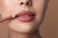 Young woman applying beautiful nude lip pencil on brown background, closeup Royalty Free Stock Photo
