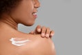 Young woman applying body cream onto back on grey background, closeup. Space for text Royalty Free Stock Photo