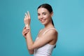 Young woman applying body cream onto her arm against turquoise background Royalty Free Stock Photo