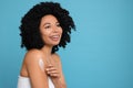 Young woman applying body cream onto shoulder on light blue background. Space for text Royalty Free Stock Photo