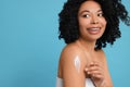 Young woman applying body cream onto shoulder on light blue background. Space for text Royalty Free Stock Photo