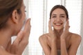 Young woman applying cleansing foam onto her face near mirror in bathroom Royalty Free Stock Photo