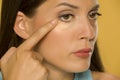 Young woman applying concealer on her low eyelids