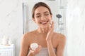 Young woman applying cream onto her face in bathroom Royalty Free Stock Photo