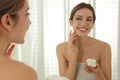 Young woman applying cream onto her face near mirror in bathroom Royalty Free Stock Photo