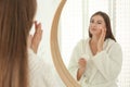 Young woman applying face cream onto her face near mirror in bathroom Royalty Free Stock Photo