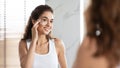 Young Woman Applying Facial Cream Moisturizing Smooth Skin In Bathroom Royalty Free Stock Photo