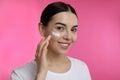 Young woman applying facial cream on pink background Royalty Free Stock Photo