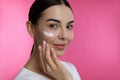 Young woman applying facial cream on pink background Royalty Free Stock Photo