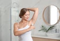 Young applying fresh roll-on deodorant to armpit in bathroom
