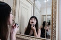 Young woman applying lipstick in front of a mirror. Girl getting ready with her makeup in a hotel bathroom. Pretty female smiling Royalty Free Stock Photo