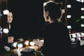 Young woman applying make up, looking herself reflection in mirror with bulbs at dressing in dark interior room. Girl applying cos Royalty Free Stock Photo