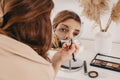 Young woman applying make-up to her face, looking at the round mirror Royalty Free Stock Photo