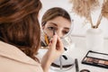 Young woman applying make-up to her face, looking at the round mirror Royalty Free Stock Photo