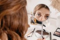 Young woman applying make-up to her face, looking at the round mirror Royalty Free Stock Photo