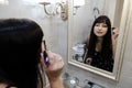 Young woman applying mascara in front of a mirror. Girl getting ready with her makeup in a hotel bathroom. Pretty female serious Royalty Free Stock Photo