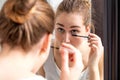 Young woman applying mascara on her lower eyelashes with mirror Royalty Free Stock Photo