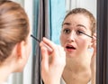 Young woman applying mascara on her top eyelashes in mirror Royalty Free Stock Photo