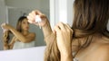 Young woman applying oil mask to hair tips in front of a mirror. Haircare concept. Focus on hair Royalty Free Stock Photo