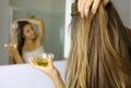 Young woman applying olive oil mask on hair in front of a mirror. Hair care concept. Focus on hair