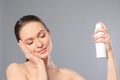 Young woman applying thermal water on face against grey background