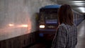 A young woman approaches the train in the subway. A girl in a coat and glasses