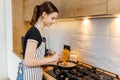 Young woman in apron cooking healthy food at modern home kitchen. Preparing meal with frying pan on gas stove. Concept of domestic Royalty Free Stock Photo