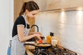 Young woman in apron cooking healthy food at modern home kitchen. Preparing pasta with frying pan on gas stove. Concept Royalty Free Stock Photo